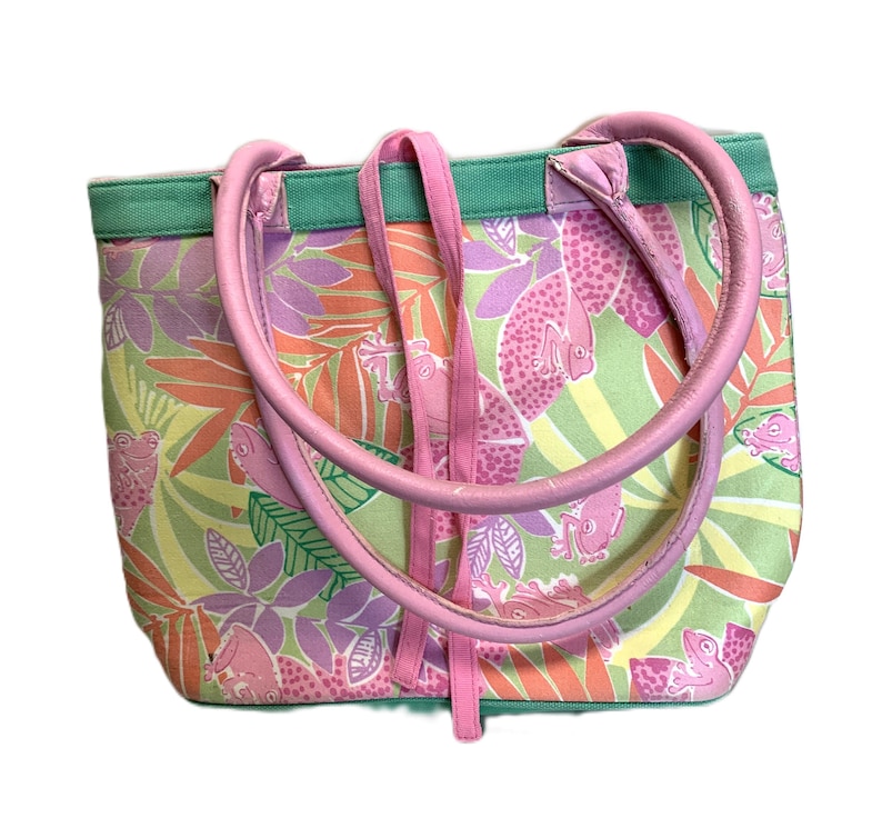 May include: A colorful tote bag with a tropical pattern featuring pink frogs, fish, and leaves. The bag has pink handles and straps, with a green trim. The bag is made of a durable fabric.