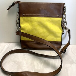May include: A brown and yellow crossbody bag with a long brown strap and silver chain accents. The bag features a yellow center panel with a subtle pattern and brown leather-like trim.