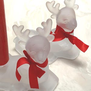 May include: Frosted glass reindeer candle holders with red ribbon scarves. The reindeer have detailed antlers and are designed to hold a single candle. A festive holiday decoration.