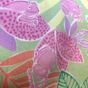 May include: A close-up of a fabric with a repeating pattern of pink frogs and leaves. The frogs are a solid pink color with darker pink spots. The leaves are green, orange, and purple. The background is a light green and yellow.