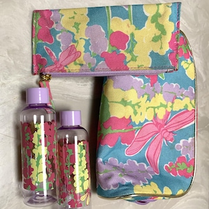 May include: A floral travel set featuring a cosmetic bag, a zippered pouch, and two clear bottles with purple lids. The set has a teal background with pink, yellow, and purple flowers and a dragonfly design.