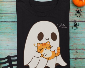 May include: Black t-shirt featuring a white ghost holding an orange tabby cat. The ghost has brown eyes and a curved mouth. A small bat outline is above the ghost. Halloween-themed design.