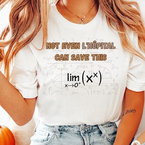 May include: White t-shirt with the text "NOT EVEN L'HÔPITAL CAN SAVE THIS" and mathematical equations. The shirt has short sleeves and a crew neck. The text is in a brown color.