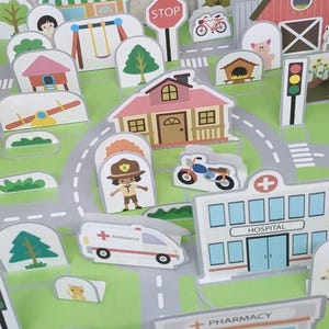 Op de afbeelding: Een kleurrijke, ge&iuml;llustreerde speelset met een stadsbeeld met gebouwen, wegen en voertuigen. Inclusief een ziekenhuis, apotheek, markt en een stopbord. De set heeft een groen- en grijskleurenschema.