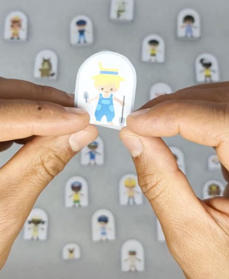 Op de afbeelding: Een sticker met een cartoonillustratie van een persoon in een blauwe overall met een schop en een troffel. De sticker wordt tussen twee handen gehouden, met andere soortgelijke stickers op de achtergrond.