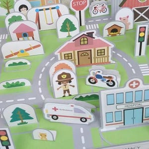 Op de afbeelding: Een kleurrijke speelgoedstadsc&egrave;ne met verschillende gebouwen, voertuigen en verkeersborden. Inclusief een markt, huizen, een ziekenhuis, een ambulance en stopborden. De sc&egrave;ne speelt zich af op een groen en grijs speelkleed.
