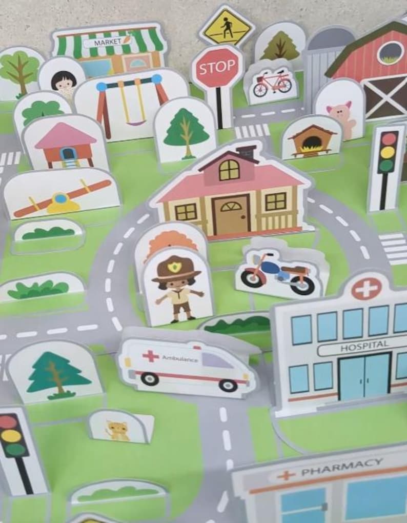Op de afbeelding: Een kleurrijke speelgoedstadsc&egrave;ne met verschillende gebouwen, voertuigen en verkeersborden. Inclusief een markt, huizen, een ziekenhuis, een ambulance en stopborden. De sc&egrave;ne speelt zich af op een groen en grijs speelkleed.