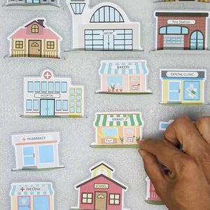 Op de afbeelding: Een verzameling kleurrijke, ge&iuml;llustreerde gebouwuitsparingen, waaronder een bank, postkantoor, luchthaven, brandweerkazerne, ziekenhuis, bakkerij, tandartspraktijk, markt, apotheek, dierenkliniek, school en politiebureau.