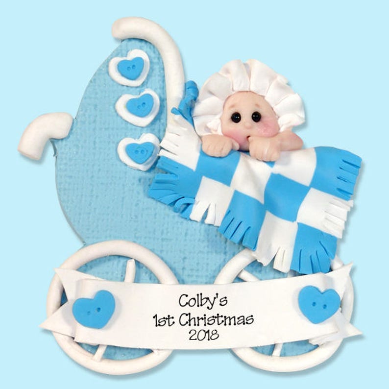 K&ouml;nnte beinhalten: Blau-wei&szlig;es Babywagen-Ornament mit einem Baby darin. Das Ornament hat ein Banner mit der Aufschrift "Colby's 1st Christmas 2018".