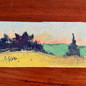 May include: Small landscape painting depicting a field and trees under a colorful sky. The artwork features a yellow field, green hills, and dark trees. The artist's signature, "A. Gore," is visible in the lower left corner. The painting is on a rectangular piece of paper.