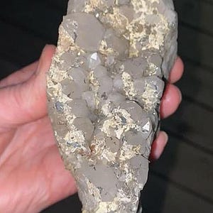 May include: A cluster of clear quartz crystals with a rough, beige matrix. The crystals are various sizes and shapes, with some appearing to be fully formed and others partially embedded. The overall shape is elongated and irregular.