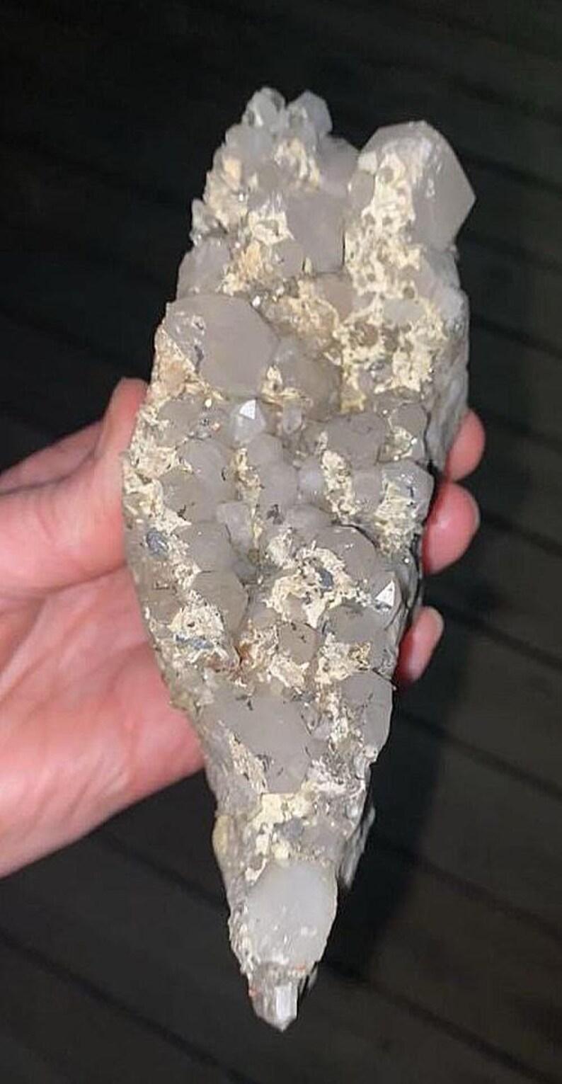 May include: A cluster of clear quartz crystals with a rough, beige matrix. The crystals are various sizes and shapes, with some appearing to be fully formed and others partially embedded. The overall shape is elongated and irregular.