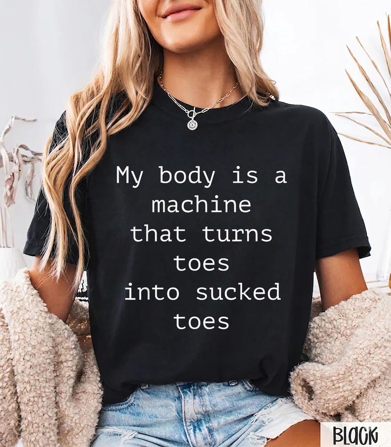 May include: Black t-shirt with the text "My body is a machine that turns toes into sucked toes" in white. The shirt is a crew neck style.