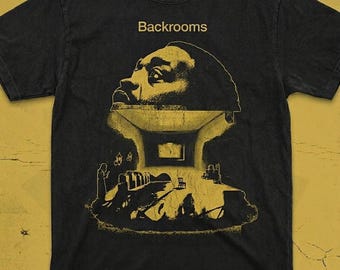 Könnte beinhalten: Ein schwarzes T-Shirt mit kurzen Ärmeln und einem gelben Grafikdruck. Das Design zeigt das Wort Backrooms über der Silhouette eines großen menschlichen Kopfes, der eine Innenszene mit einem Stuhl und architektonischen Elementen enthält.