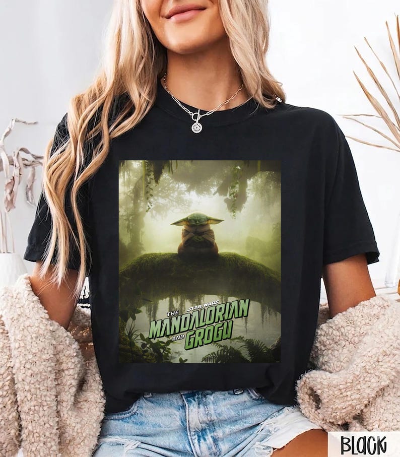K&ouml;nnte beinhalten: Schwarzes T-Shirt mit einer Grafik von The Mandalorian und Grogu. Das Design zeigt Grogu in einer Waldszene. Der Text "The Mandalorian and Grogu" ist in Gr&uuml;n und Wei&szlig;. Das Shirt ist ein l&auml;ssiger Stil.