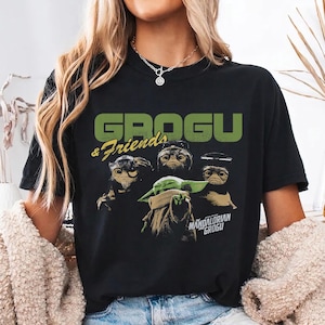 Peut inclure: T-shirt noir avec un motif de Grogu et de trois autres cr&eacute;atures, avec le texte "GROGU & Friends" en vert au-dessus de l'image. En dessous de l'image se trouve le texte "MANDALORIAN GROGU".