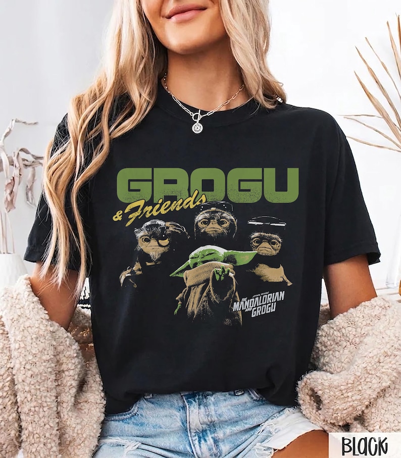 Peut inclure: T-shirt noir avec un motif de Grogu et de trois autres cr&eacute;atures, avec le texte "GROGU & Friends" en vert au-dessus de l'image. En dessous de l'image se trouve le texte "MANDALORIAN GROGU".