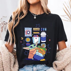 May include: Black t-shirt with a cartoon illustration of a character holding a sandwich, surrounded by food items. The design includes a blue, green, orange, and purple color palette. The word "BLACK" is printed at the bottom right.