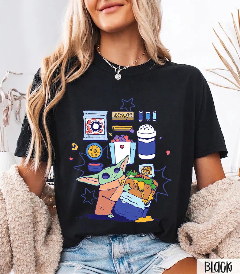 May include: Black t-shirt with a cartoon illustration of a character holding a sandwich, surrounded by food items. The design includes a blue, green, orange, and purple color palette. The word "BLACK" is printed at the bottom right.