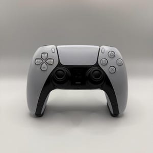 Pode incluir: Um controle de jogo sem fio branco e preto com um design simétrico. O controle possui um touchpad, botões direcionais e botões de ação. O controle tem uma estética elegante e moderna.