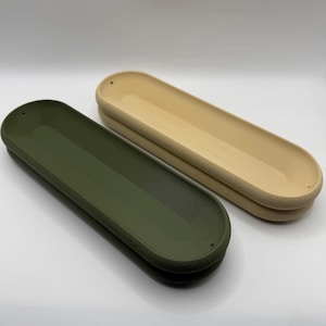 May include: Two long, oval-shaped trays. One is olive green, the other is a light beige. Both have a textured, ridged border and a smooth, recessed interior. The trays are designed with small holes at each end.
