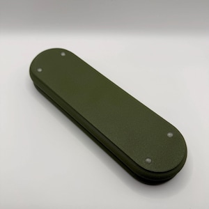 May include: An olive green, rectangular object with rounded ends. The object appears to be made of a solid material and has three small, silver-colored rivets on the top surface. The item is a solid color and has a matte finish.