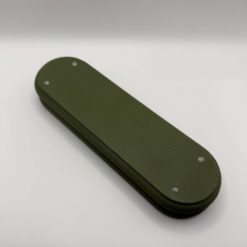 May include: An olive green, rectangular object with rounded ends. The object appears to be made of a solid material and has three small, silver-colored rivets on the top surface. The item is a solid color and has a matte finish.