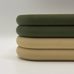May include: Close-up of three stacked, textured, round objects. The top two are olive green, and the bottom one is tan. The objects have a smooth, rounded edge and a slightly rough surface.