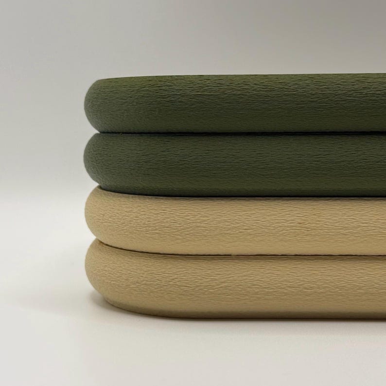 May include: Close-up of three stacked, textured, round objects. The top two are olive green, and the bottom one is tan. The objects have a smooth, rounded edge and a slightly rough surface.