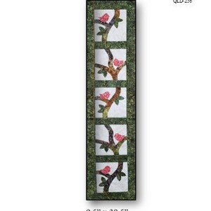 Puede incluir: Un patrón de acolchado para un camino de mesa o una pared colgante llamado "Perched". El patrón presenta un diseño de pájaros posados ​​en ramas con flores rosas. El patrón mide 24,1 cm por 100,3 cm.
