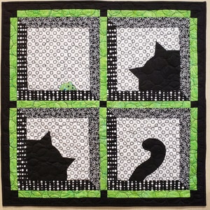 May include: A black and white quilt with four squares. Each square has a black cat silhouette on a white background with black polka dots. The squares are framed with a green border.