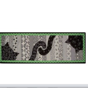 Könnte beinhalten: Eine schwarz-weiße Quiltdecke mit grünem Punktmuster-Rand. Die Decke zeigt ein Design aus zwei schwarzen Katzen, deren Schwänze ineinander verschlungen sind.