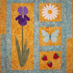 May include: A quilted wall hanging with a blue and white floral design. The design features a purple iris, a white daisy, a blue butterfly, and red strawberries.