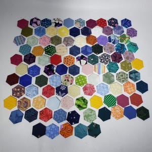 May include: A collection of colorful, hexagonal fabric pieces arranged in a honeycomb pattern. The patchwork includes various patterns and colors, such as floral, polka dots, and geometric designs. The fabric pieces are in shades of blue, green, yellow, red, and purple.