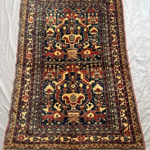 Könnte beinhalten: Ein rechteckiger Teppich mit einem dunkelblauen Mittelfeld und zwei symmetrischen Medaillons in Rot und Creme. Der Teppich ist mit komplexen geometrischen und floralen Motiven verziert und von einer breiten Bordüre mit Mustern und Fransen umrandet.