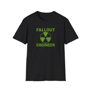 May include: A black short-sleeved t-shirt featuring a green graphic print on the chest. The design includes a circular radiation hazard symbol centred between the words FALLOUT and ENGINEER, both printed in a bold, distressed green font.