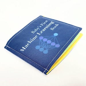 Könnte beinhalten: Ein blaues Stoffbuch mit dem Titel "Baby's First Machine Learning Book" und einer Grafik eines neuronalen Netzwerks. Das Buch hat gelbe und grüne Stoffkanten.