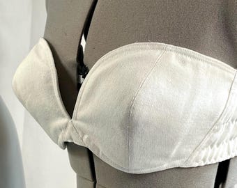 May include: A strapless off-white top featuring a structured sweetheart neckline and a visible vertical ribbed texture. The garment is displayed on a grey mannequin torso, showcasing the fitted bodice design and the clean, neutral fabric finish.