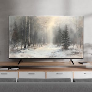 Peut inclure: Un grand écran plat affiche une scène paisible de forêt hivernale. L'œuvre d'art représente un sentier enneigé serpentant à travers une forêt brumeuse avec de grands arbres. Le téléviseur est sur un meuble en bois clair avec des tiroirs blancs, avec des plantes en pot.