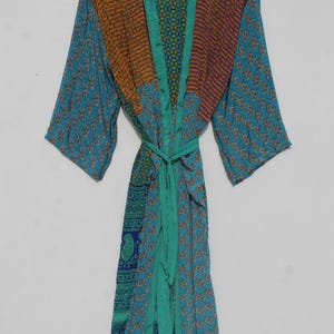 May include: A colorful, patterned robe with a tie waist. The robe features a mix of teal, orange, and purple fabrics. The robe is hanging on a wooden hanger against a plain white background. The robe is a bohemian style.