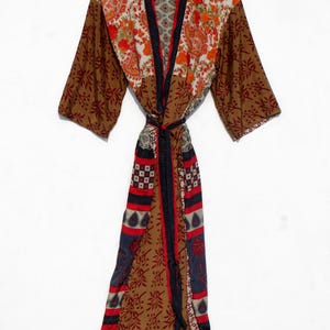 May include: A long, patterned robe with a tie waist. The robe features a mix of floral and paisley patterns in shades of brown, orange, red, and blue. The robe has long sleeves and a black trim.