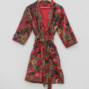 以下が含まれることがあります： 赤い花柄のローブと、お揃いのベルト。ローブは、赤、緑、黄色、茶色の花と葉の鮮やかな模様が特徴です。木製のハンガーにかかっています。