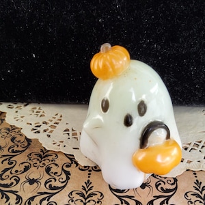 Può includere: Piccola statuina a forma di fantasma bianco con occhi neri e una piccola zucca arancione sulla testa. Il fantasma tiene in mano una borsa arancione per dolcetti. Decorazione di Halloween.