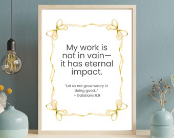 Può includere: Stampa incorniciata con il testo "Il mio lavoro non è vano - ha un impatto eterno". La citazione è circondata da un disegno a nastro dorato. La stampa è in una cornice di legno chiaro e poggia su una superficie bianca.