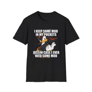 Könnte beinhalten: Schwarzes T-Shirt mit einer Cartoonfigur und dem Text "I KEEP SOME MUD IN MY POCKETS JUST IN CASE I EVER NEED SOME MUD". Die Grafik ist in Weiß, Rot, Gelb und Schwarz gehalten.