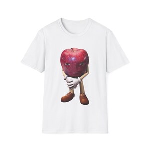 May include: White t-shirt featuring a cartoon apple character with a stern expression. The apple has a red and purple hue, wearing white gloves and brown shoes. The design is centered on the shirt.