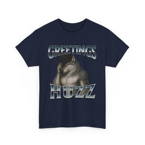Op de afbeelding: Marineblauw T-shirt met de tekst "GREETINGS HUZZ" en een illustratie van een wolf met een hoed. De wolf is realistisch weergegeven. Het T-shirt heeft een ronde hals en korte mouwen.