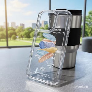 Könnte beinhalten: Transparente Handyhülle mit einem farbenfrohen abstrakten Design aus blauen, orangefarbenen und gelben Pinselstrichen. Auf der Hülle stehen die Wörter "colour", "The gment" und "colour". Hinter der Hülle befindet sich ein Edelstahl-Reisebecher mit schwarzem Band.