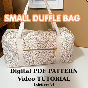 May include: A small duffle bag featuring a white fabric with a delicate floral pattern of tiny pink flowers and green leaves. The bag has cream-coloured webbing straps, gold-tone zippers, and the text SMALL DUFFLE BAG, Digital PDF PATTERN, Video TUTORIAL, Usletter+A4.