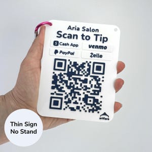 May include: A white rectangular sign with the text "Aria Salon Scan to Tip" and payment options. Includes QR codes and the text "Thin Sign No Stand". A pink carabiner clip is attached.